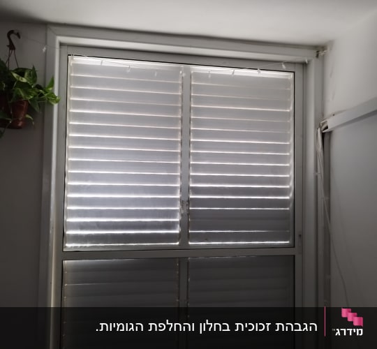 חלון עם תריסים סגורים בחדר מואר חלקית